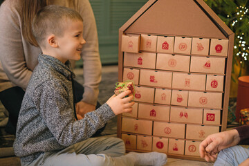 A child opens a box with a surprise Advent calendar surrounded by parents sitting on the floor by a Christmas tree