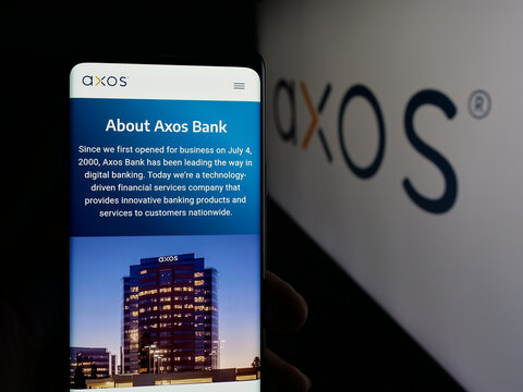 Stuttgart, Germany - 10-04-2025: Person holding cellphone with webpage of US banking company Axos Financial Inc. on screen in front of logo. Focus on center of phone display.