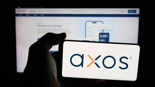 Stuttgart, Germany - 10-04-2025: Person holding mobile phone with logo of US banking company Axos Financial Inc. on screen in front of web page. Focus on phone display.