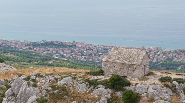 Ancient stone chapel on a coastal mountain ridge with panoramic sea view of the Dalmatian coast.