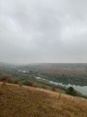 Misty autumn morning with fog over a calm pond surrounded by colorful trees on gentle hills. Peaceful natural landscape in soft light.