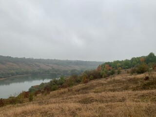 Misty autumn morning with fog over a calm pond surrounded by colorful trees on gentle hills. Peaceful natural landscape in soft light.