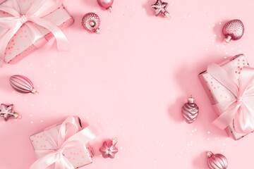 Festive pink Christmas composition with gift box, ribbon and shiny baubles creating a bright frame on pastel background. Cheerful and elegant image perfect for greeting cards, posters and design.