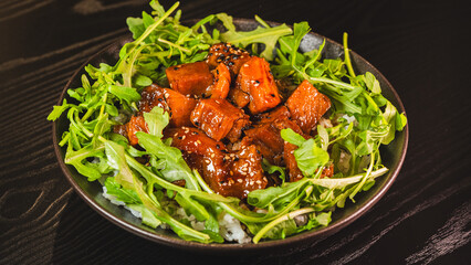 A vibrant bowl of sticky soy-honey glazed pork served over oriental rice with fresh rocket leaves. The peppery greens perfectly complement the sweet-savory pork and sesame topping.
