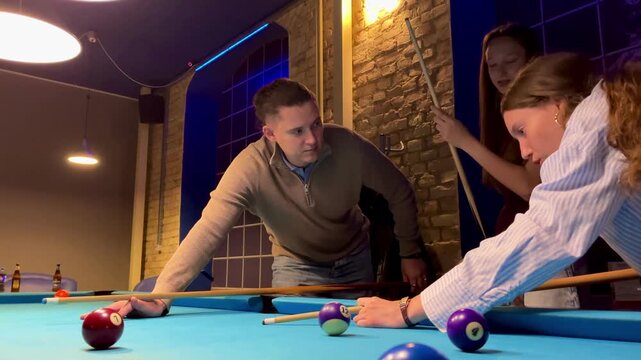Father and teenagers play billiards. The father teaches his daughters to play billiards. The concept of parents and children, upbringing, family rest.