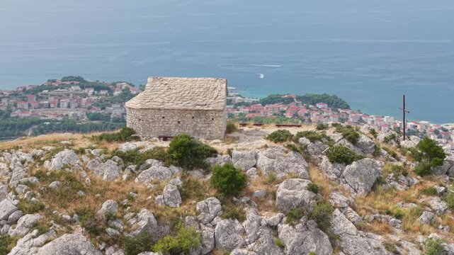 Ancient stone chapel on a coastal mountain ridge with panoramic sea view of the Dalmatian coast.