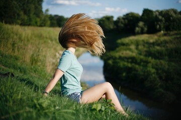 Fototapeta premium Long blonde haired woman doing harflip in the grass next to river with hair covering her face