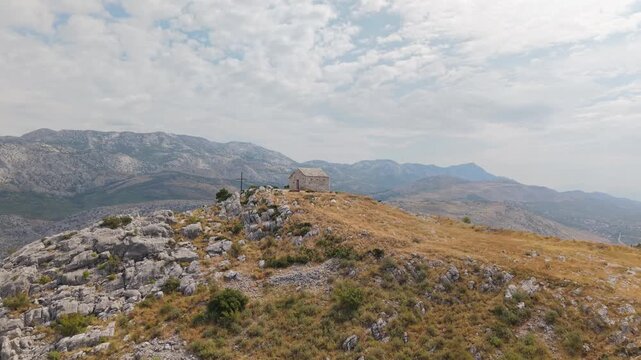 Ancient stone chapel on a coastal mountain ridge with panoramic sea view of the Dalmatian coast.