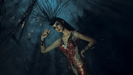 Young woman dressed as a witch in red dress performing a ritual to summon spirits on Halloween in a dark room (noise) surrounded by candles. Halloween festival concept.