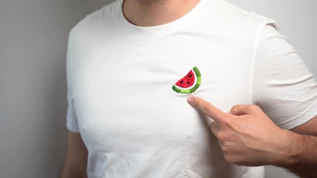 Stand with Palestine. Young man points to watermelon symbol embroided in t-shirt