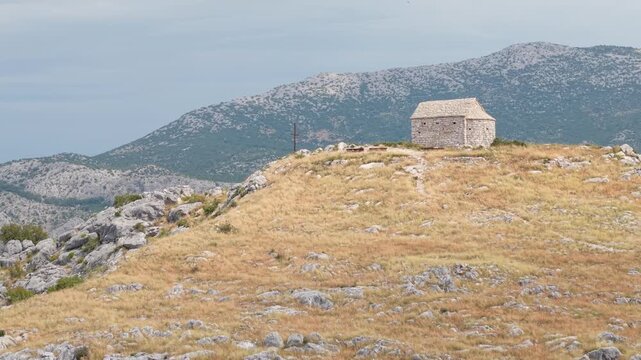 Ancient stone chapel on a coastal mountain ridge with panoramic sea view of the Dalmatian coast.