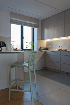 Modern kitchen interior with grey kitchen countertop with mint chair, kitchen sink with faucet by the window. Tiled floor in dining room. Verticle.