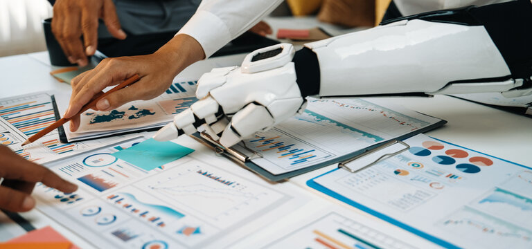 A robotic arm engages with data analysis on printed reports, showcasing a blend of human and machine collaboration in a vibrant office setting.Noogenesis