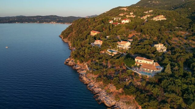 Aerial view of coastal villas nestled among lush greenery, showcasing serene waters and rocky shoreline, capturing the tranquil beauty of a picturesque seaside retreat