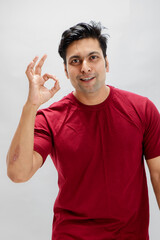 Fototapeta premium A cheerful man in a red t-shirt showing the OK hand gesture with confidence and positivity. Studio portrait on a white background, conveys positivity, friendly communication, and success.
