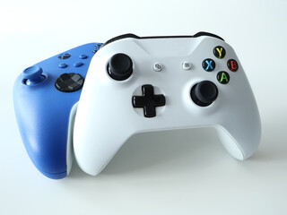 Two wireless game controllers, a white one in front with a blue behind, create a dynamic gaming setup. Ideal stock image for gaming, technology, and entertainment themes.