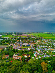 Aerial view of grid pattern residential zone with canal, gardens, and farmland contrasting compact housing with expansive green fields under dramatic overcast skies.