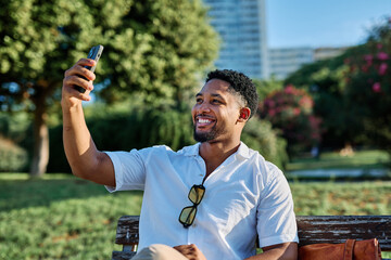 Young man enjoys sunny day while using smartphone and making a selfie photo in urban setting, highlighting his joy and connection to the world around him