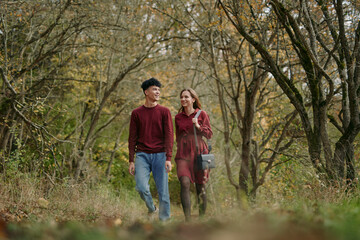 Fototapeta premium A candid scene shows a couple walking through a sunlit forest, conveying authentic connection and genuine emotion as they share a quiet smile amid tall trees.
