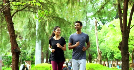 Indian young couple jogging in park together enjoying healthy morning routine and fitness oriented start of the day, spending quality time outdoors breathing fresh air surrounded in sunshine