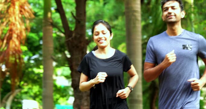 Indian young couple jogging in park together enjoying healthy morning routine and fitness oriented start of the day, spending quality time outdoors breathing fresh air surrounded in sunshine
