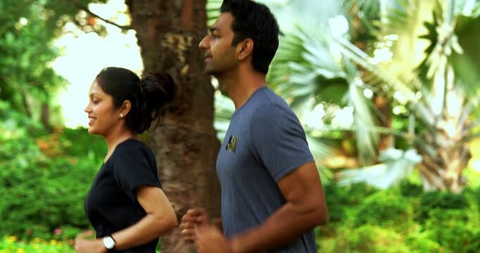 Indian young couple jogging in park together enjoying healthy morning routine and fitness oriented start of the day, spending quality time outdoors breathing fresh air surrounded in sunshine