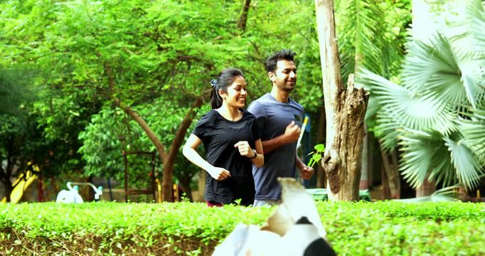 Indian young couple jogging in park together enjoying healthy morning routine and fitness oriented start of the day, spending quality time outdoors breathing fresh air surrounded in sunshine