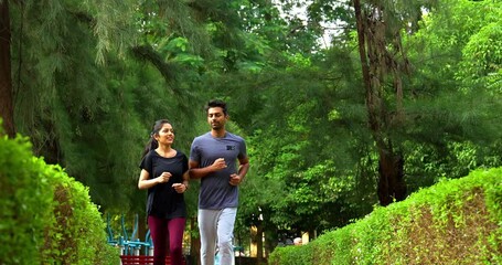 Indian young couple jogging in park together enjoying healthy morning routine and fitness oriented start of the day, spending quality time outdoors breathing fresh air surrounded in sunshine