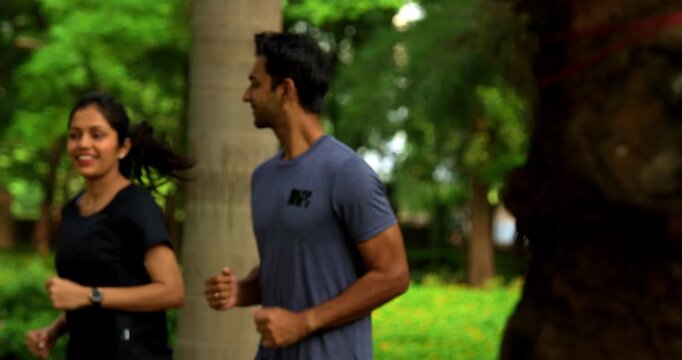 Indian young couple jogging in park together enjoying healthy morning routine and fitness oriented start of the day, spending quality time outdoors breathing fresh air surrounded in sunshine