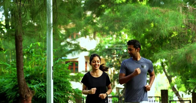 Indian young couple jogging in park together enjoying healthy morning routine and fitness oriented start of the day, spending quality time outdoors breathing fresh air surrounded in sunshine