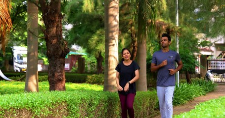 Indian young couple jogging in park together enjoying healthy morning routine and fitness oriented start of the day, spending quality time outdoors breathing fresh air surrounded in sunshine