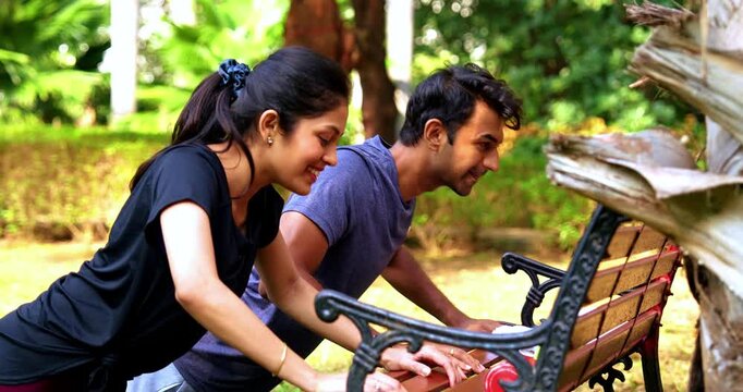 Indian beautiful young couple doing pushups on bench in park outdoors during morning fitness session, showing strength, teamwork, and healthy lifestyle while enjoying sunlight, fresh air, greenery
