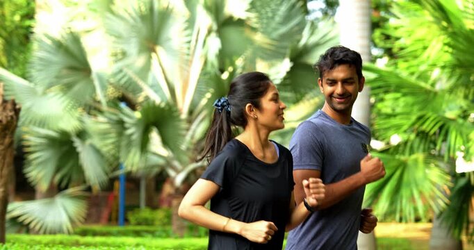 Indian young couple jogging in park together enjoying healthy morning routine and fitness oriented start of the day, spending quality time outdoors breathing fresh air surrounded in sunshine