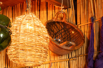 A lamp and a bowl are hanging from a bamboo wall. The bowl is made of clay and has a black....