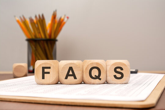 Wooden cubes spelling FAQs on wooden desk with plant background