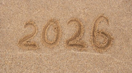The numbers 2026 are written on beige sand. The concept of New Year and Christmas.