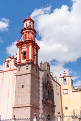 Fototapeta premium A large building with a red roof and a clock tower. The building is surrounded by a fence. Historic center of Queretaro, colonial architecture, decorations for the celebration of Mexico's Independence