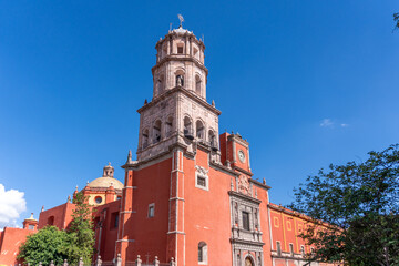 Obraz premium A beautiful red building with a tall tower and a blue sky in the background. Historic center of Queretaro, colonial architecture, decorations for the celebration of Mexico's Independence Day.