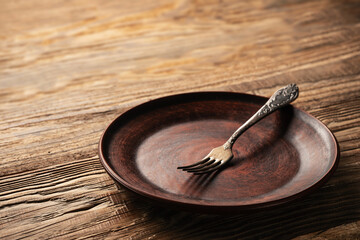Fork placed on a rustic wooden plate on a textured table surface showcasing minimalism and simplicity in dining