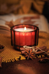Hand lighting red candle with match surrounded by dried leaves open book cinnamon and yellow fabric