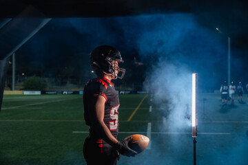 American football player entering field at night with smoke