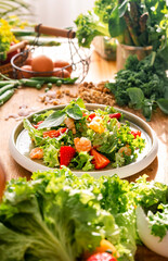 Delicious green salad with lettuce, strawberry, shrimps and nuts on oak table in bright cozy kitchen
