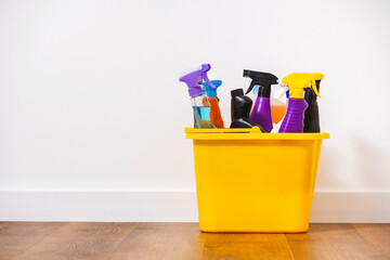 Bright multi-colored cleaning products, household chemicals bottles and sprays, rags, sponges in orange bucket for washing, wiping and dusting