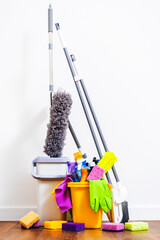 Cleaning products, household chemicals bottles and sprays, rags, sponges in orange bucket for washing the floor, brushes, broom for wiping and dusting