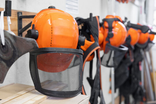 Reihe von orangefarbenen Schutzhelmen mit Visier und Geh&ouml;rschutz h&auml;ngt ordentlich an einer Wand. Das Motiv steht f&uuml;r Arbeitssicherheit, Forst- und Handwerksberufe sowie professionelle Schutzausr&uuml;stung