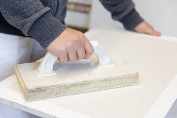 Hand gl&auml;ttet frischen Putz mit Gl&auml;ttekelle &ndash; detailreiche Nahaufnahme eines handwerklichen Arbeitsschritts bei Renovierung und Innenausbau.