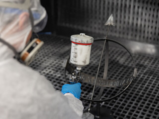 Person in Schutzkleidung arbeitet in einer technischen Kabine und reinigt bzw. beschichtet ein Bauteil mit professioneller Ausr&uuml;stung. Das Motiv steht f&uuml;r Arbeitssicherheit, Industrieprozesse und pr&auml;z