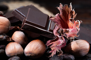 Broken dark chocolate with cocoa beans and hazelnuts on a wooden table