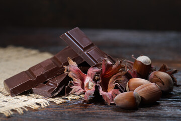 Broken dark chocolate with cocoa beans and hazelnuts on a wooden table