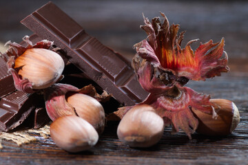 Broken dark chocolate with cocoa beans and hazelnuts on a wooden table